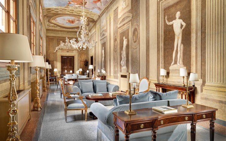 Grand classical hall with frescoed ceilings, classical statues, and plush blue seating. Old Money Hotels in Italy