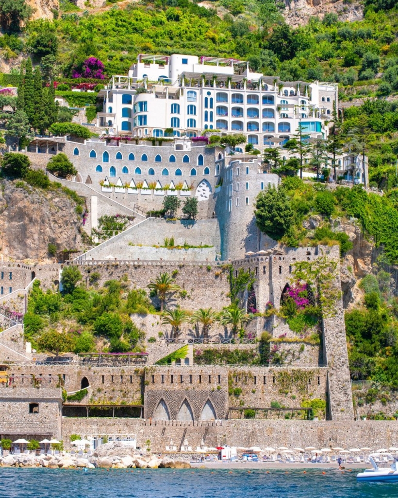 Cliffside luxury hotel built into steep coastal rocks with arched stone terraces. Old Money Hotels in Italy