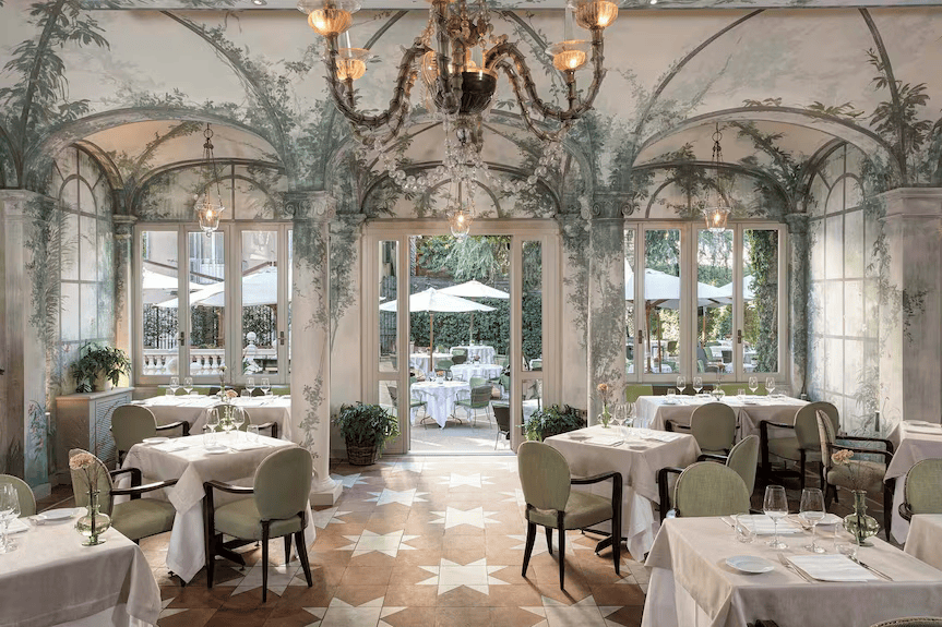 Elegant indoor dining room with painted garden murals and arched glass doors. Old Money Hotels in Italy