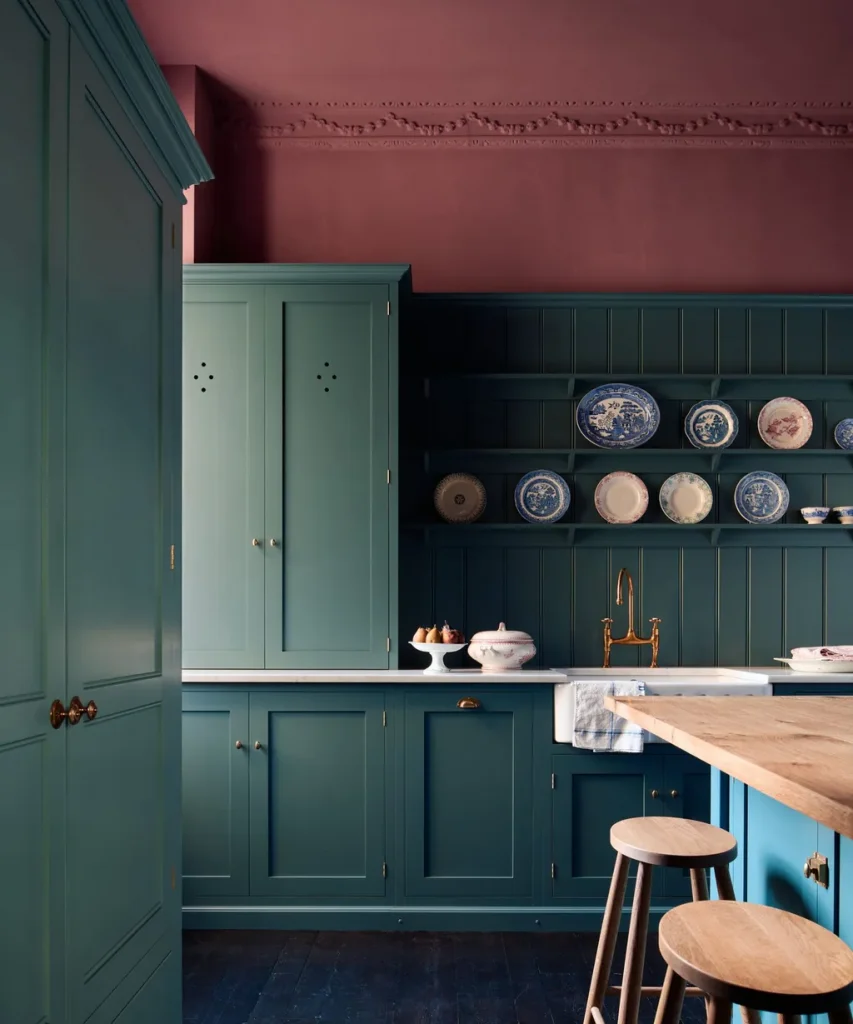 Classic dark green kitchen with terracotta-pink wall, open shelving displaying blue and white china, and a brass tap - fall winter 2027 trends