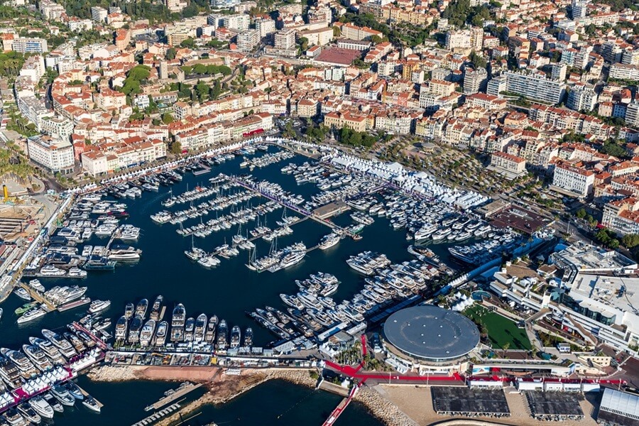 A high-angle bird's-eye view of the historic port filled with docked boats and exhibition structures during the Cannes Yachting Festival 2026.
