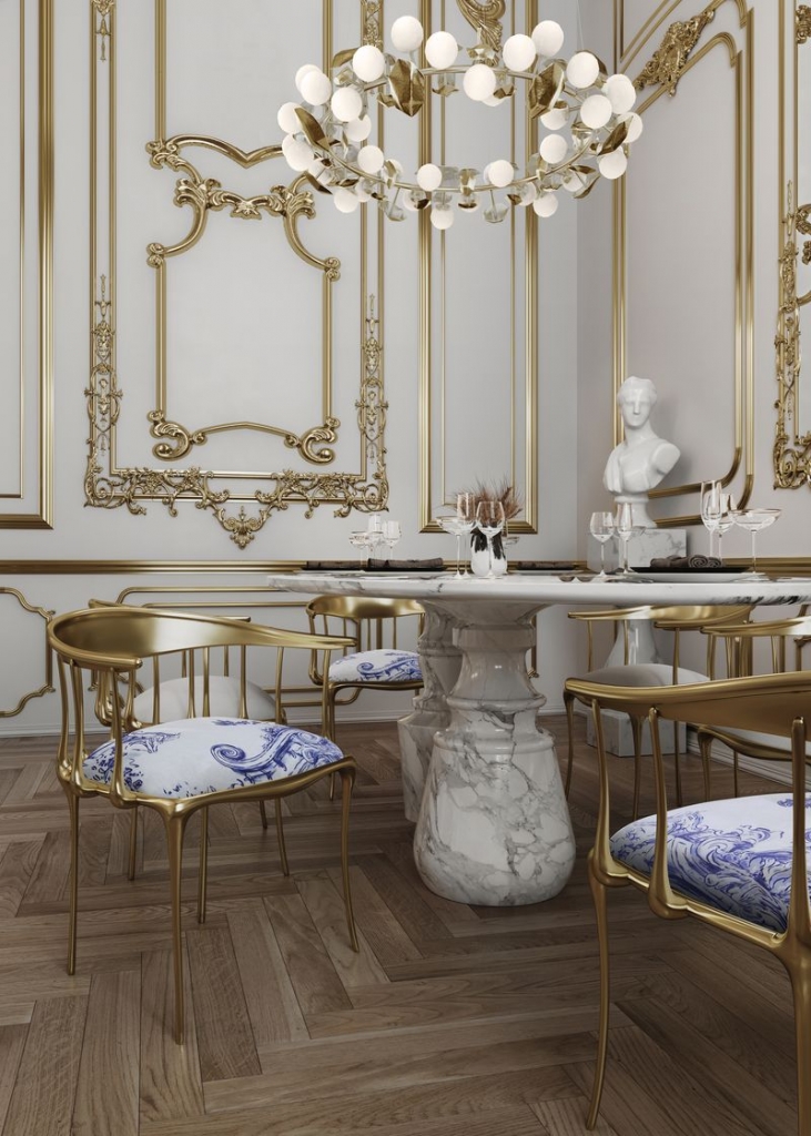 Elegant dining room with gilded wall mouldings, marble pedestal table and gold chairs with blue and white patterned seats - fall winter 2027 trends