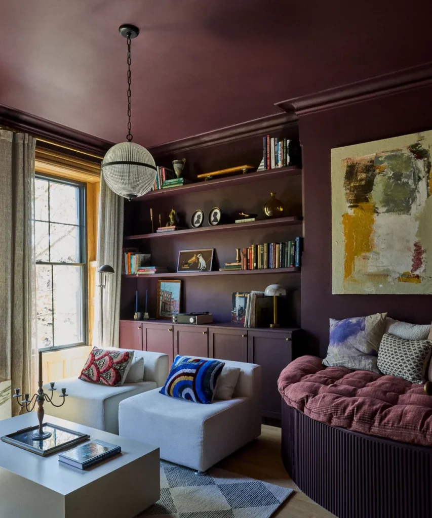 Plum and burgundy-toned living room with built-in bookshelves, light grey sofas and colorful throw pillows - fall winter 2027 trends