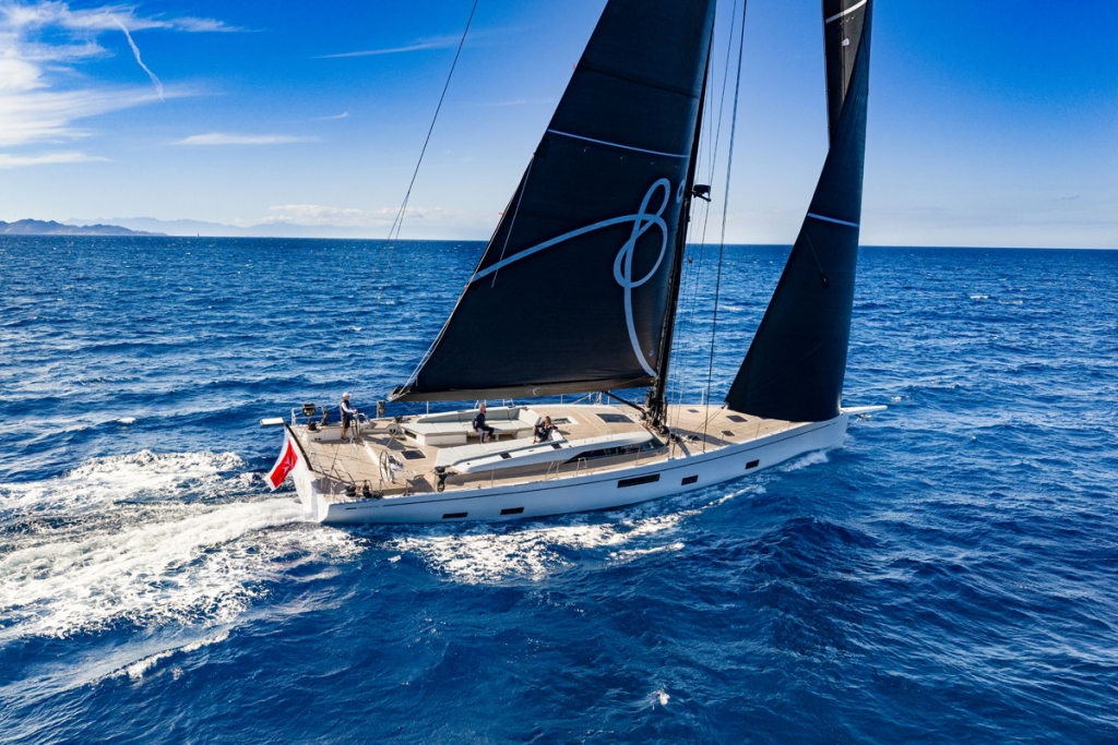 A modern sailing yacht navigating through deep blue ocean waters with large black sails up at the Cannes Yachting Festival 2026.