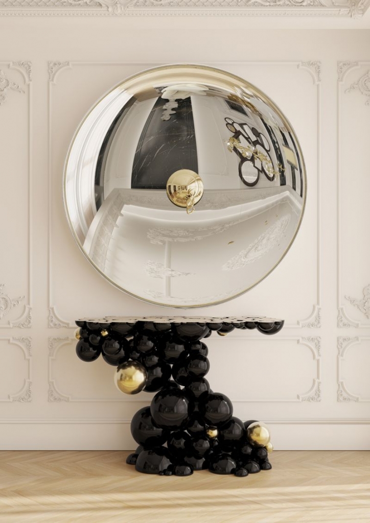 Black console table with black and gold spheres beneath a round convex mirror in a gold frame - fall winter 2027 trends