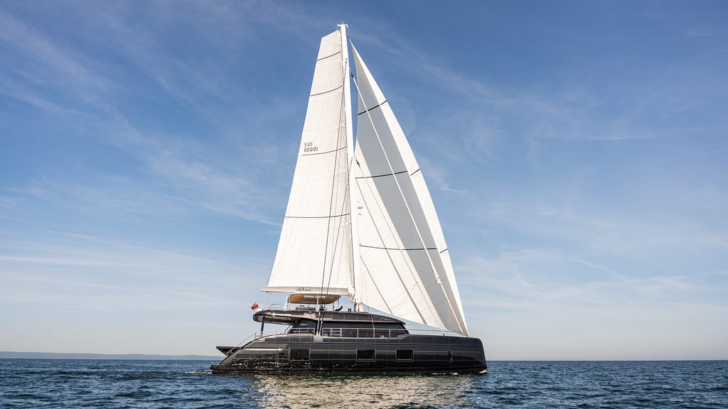 Sleek modern catamaran sailboat navigating the open sea with large white sails deployed under a clear blue sky, Monaco Yacht Show 2026