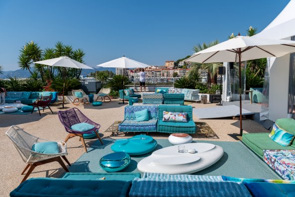 An upscale outdoor lounge terrace featuring vibrant teal and blue seating, modern white coffee tables, and sun umbrellas at the Cannes Yachting Festival 2026.