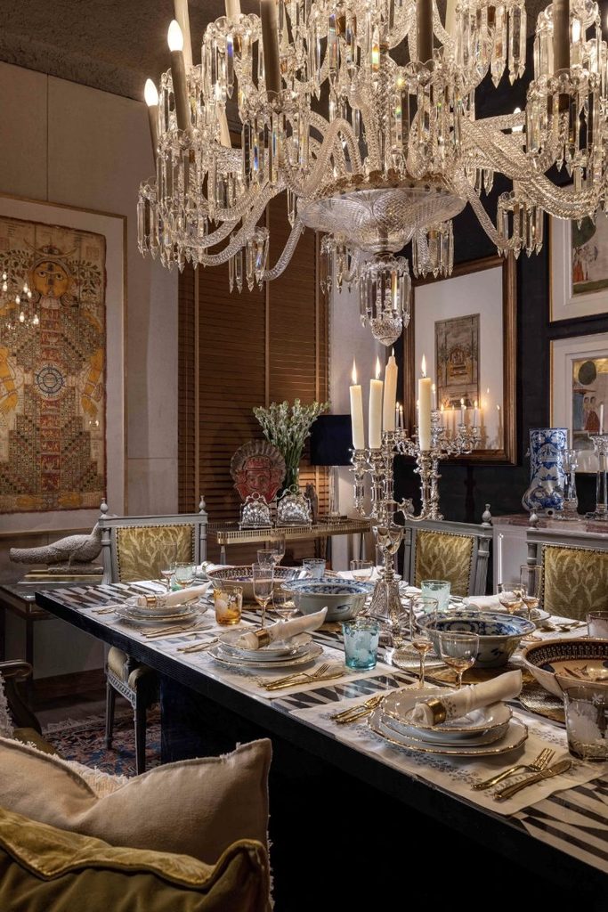 Elegant dining room featuring a grand crystal chandelier above a long banquet table set with porcelain plates, glassware, napkins, and a lighted crystal candelabra.