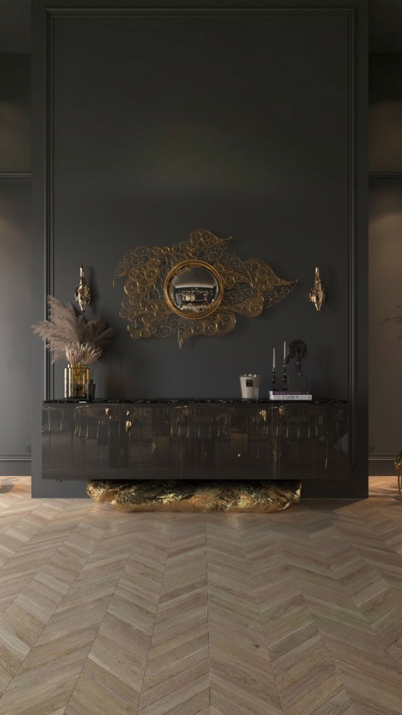 Glossy black Angra sideboard with a sculptural molten gold rock-like base, beneath a gold filigree convex mirror in a dark moody room – statement sideboard.Glossy black Angra sideboard with a sculptural molten gold rock-like base, beneath a gold filigree convex mirror in a dark moody room – statement sideboard.