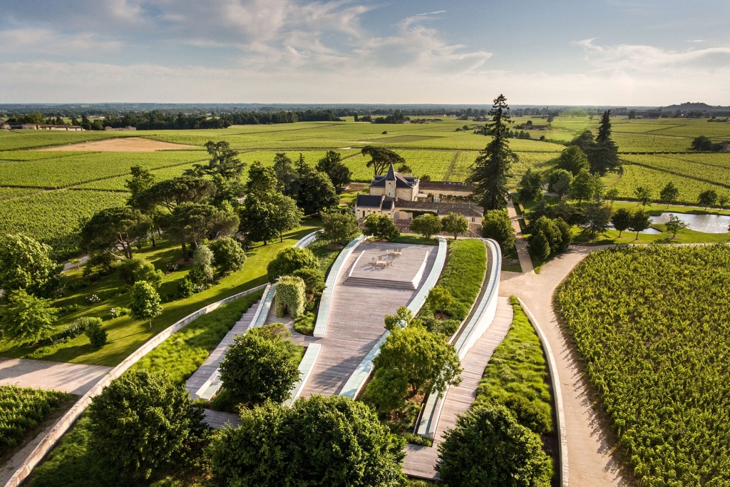 High-angle view of a modern wave-shaped architectural structure integrated into a vast green vineyard landscape, prestigious wine estates