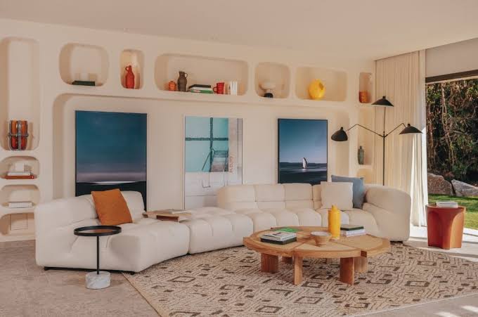 A cozy, modern lounge space with built-in wall niches, a plush modular cream sofa, a circular wooden coffee table, and abstract artwork at luxury furniture showrooms in Monaco.