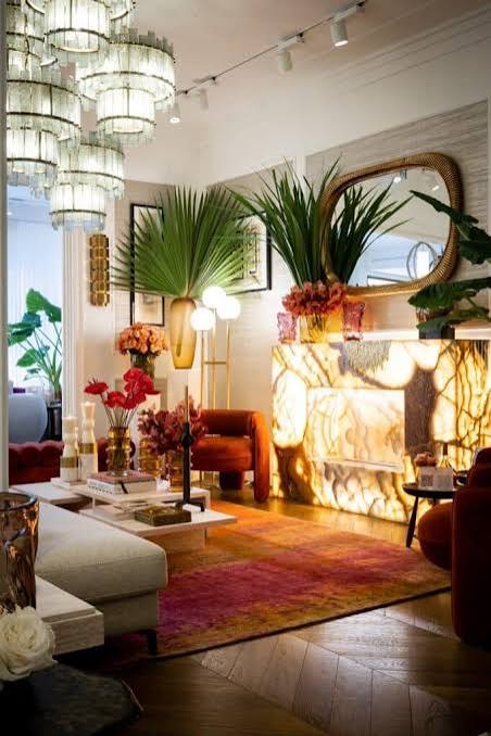 A vibrant living space featuring a glowing onyx fireplace, rich red and orange accents, lush tropical plants, and crystal chandeliers at luxury furniture showrooms in Monaco.