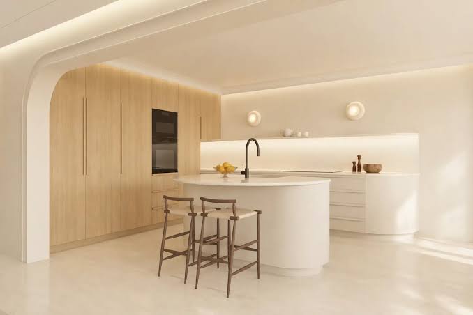 A clean, minimalist kitchen featuring light wood cabinetry, a curved central island with a sleek black faucet, and matching bar stools at luxury furniture showrooms in Monaco.