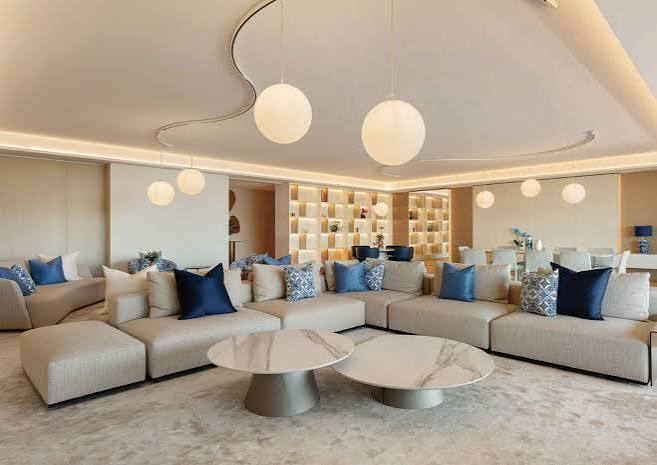 A spacious contemporary living room with a large neutral sectional sofa, circular marble coffee tables, and unique globe pendant lights, showcased at luxury furniture showrooms in Monaco.