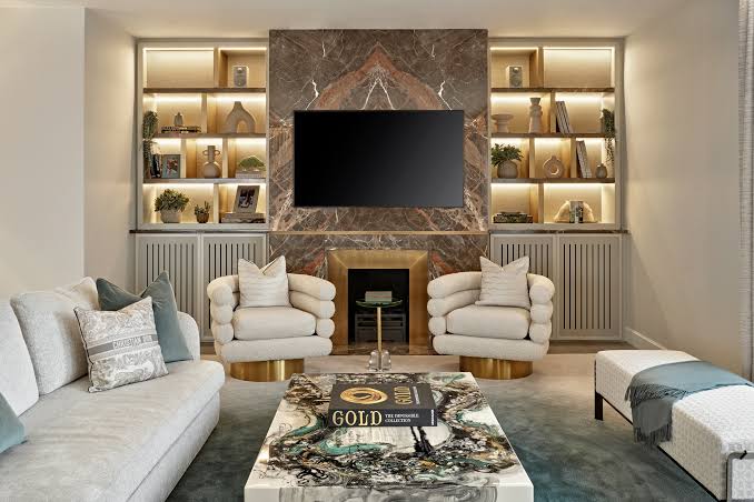 A modern luxury living room featuring a patterned marble coffee table, cream swivel armchairs, and a built-in media wall with warm recessed shelving, displayed at luxury furniture showrooms in Monaco.