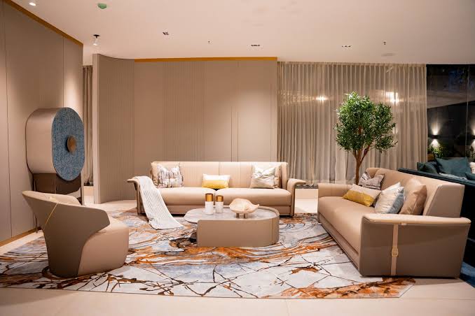 A contemporary seating arrangement with a beige sectional sofa, a matching armchair, a curved central coffee table, and a decorative blue circular cabinet at luxury furniture showrooms in Hyderabad.