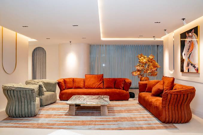 A warm, modern living area styled with vibrant orange-red velvet sofas, a patterned marble coffee table, and a large statement artwork of a horse on the wall at luxury furniture showrooms in Hyderabad.