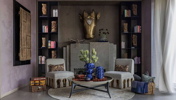 A sophisticated living space featuring a gold bull head sculpture mounted on a wood-paneled wall, flanked by black bookshelves, with two cream armchairs and a central coffee table at luxury furniture showrooms in Hyderabad.