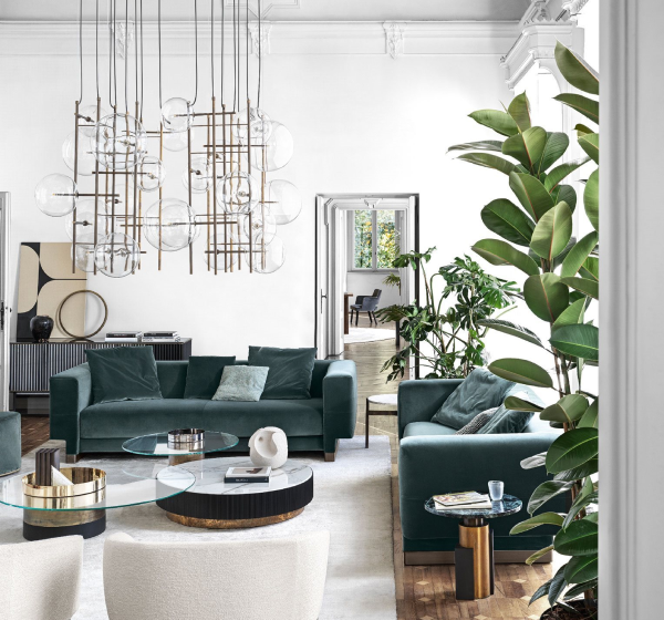 A stylish open-concept lounge featuring dark teal velvet sofas, a striking modern geometric bubble chandelier, and lush indoor potted plants at luxury furniture showrooms in Hyderabad.