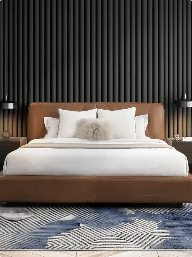 A modern king-size bed with a rich brown leather headboard and frame, styled with white linens and a textured grey accent pillow against a dark fluted wall panel, displayed at luxury furniture showrooms in Hyderabad.