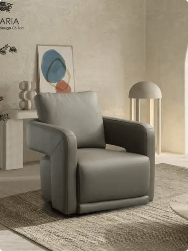 A sleek grey leather armchair with a curved frame and matching back cushion, set on a textured rug in a minimalist room with abstract wall art at luxury furniture showrooms in Hyderabad.